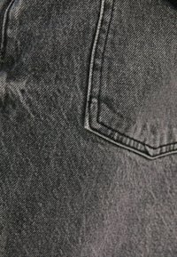 Tmavě šedá džínová tkanina s mírně strukturovaným povrchem. Má zadní kapsu s kontrastním šitím a čistý, jednoduchý design.