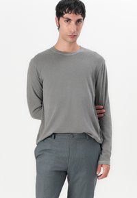 Lange mouwen, lichtgrijs shirt van zachte stof, met een ronde halslijn en een relaxte pasvorm, gecombineerd met grijze getextureerde broek met voorknopen.