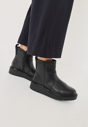 Sorte læder ankelstøvler med flad sål, sidelukning med lynlås og trækstrop; glat tekstur med syningsdetaljer og minimalistisk design.