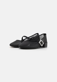 Black flats made of textured fabric with a low heel, featuring a decorative silver buckle on the strap. Pointed toe design.