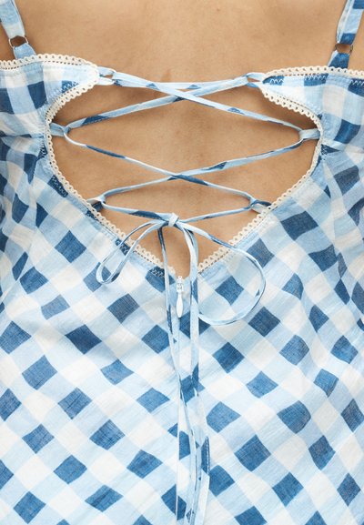 Μπλε και λευκό φόρεμα με καρό μοτίβο στο πίσω μέρος, με λεπτές διασταυρωμένες τιράντες δεμένες σε φιόγκο πάνω από ένα φερμουάρ και τελειώματα με δαντέλα.