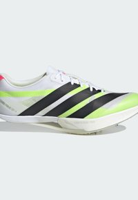 Chaussure de sport blanche avec une tige texturée, présentant des rayures diagonales noires et vert néon, et des crampons en caoutchouc sur la semelle extérieure pour la traction.