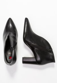 Bottes courtes à talons hauts noires en cuir, avec un bout pointu et une fermeture éclair latérale. Talon carré à surface lisse et détails minimaux.