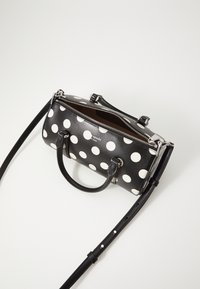 Black leather handbag with white polka dots, dual handles, adjustable strap, and silver zipper. Interior reveals a brown lining.