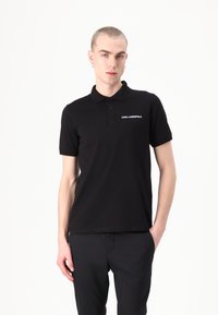 Polo nero con colletto classico, maniche corte e un piccolo logo bianco sul petto. Realizzato in tessuto liscio con una vestibilità regolare.