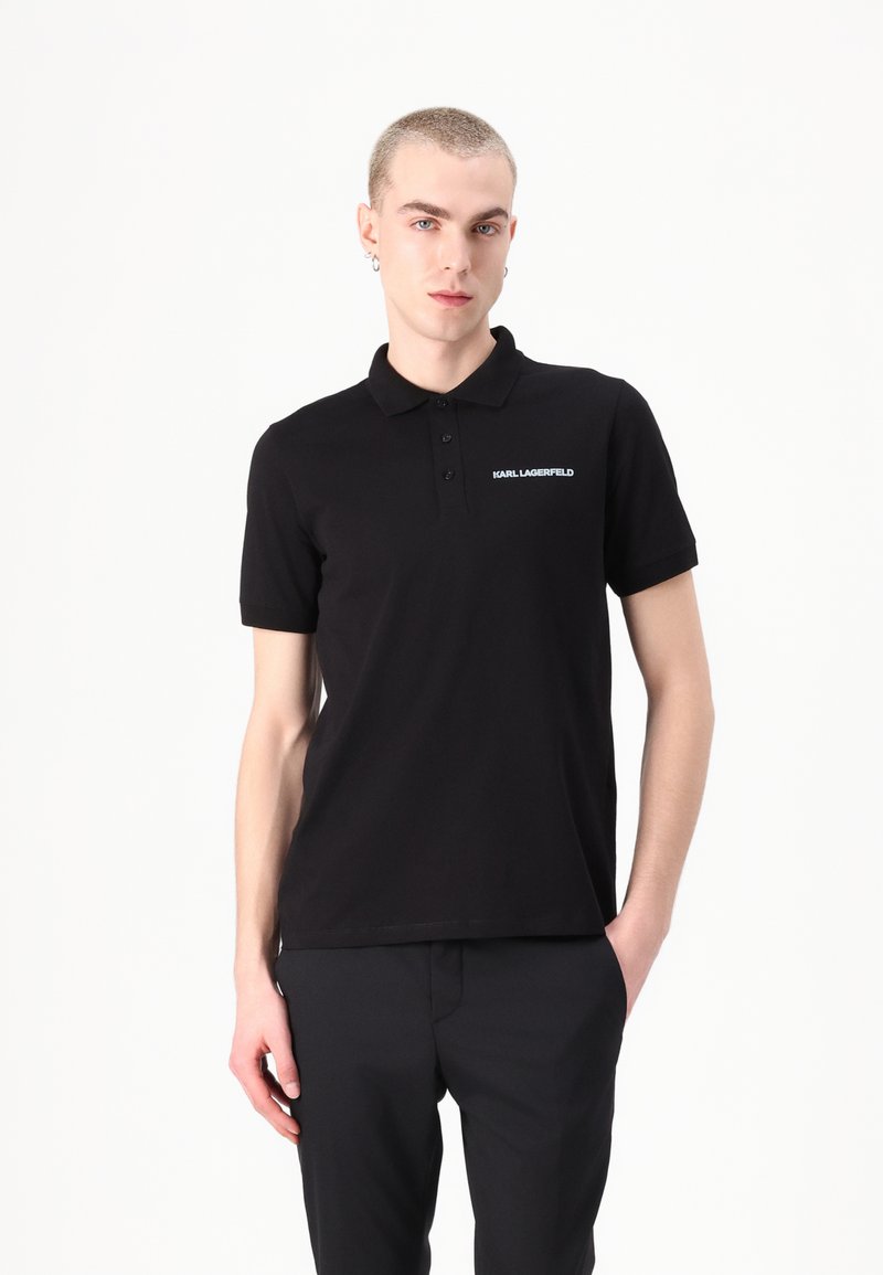Polo nero con colletto classico, maniche corte e un piccolo logo bianco sul petto. Realizzato in tessuto liscio con una vestibilità regolare.