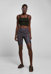 Top corto nero, pantaloni da bici a motivi con design di scorpione in grigio scuro e sandali neri. Il tessuto sembra liscio con un taglio aderente.