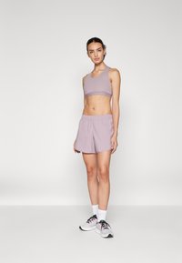 Ensemble de brassière de sport et de shorts lilas, doté d'une texture lisse, d'une taille élastique et d'un tissu léger, associé à des chaussures de sport blanches.