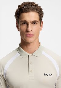 Light beige polo shirt with short sleeves and white side accents. Features a standard collar and a black "BOSS" logo on the chest.