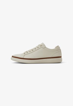 Beige sneakers gjorda av texturerat syntetiskt material, med ett brunt märke, snörning, rund tå och en dämpad sula.