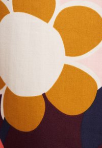 Ein Stoff mit einem großen, abstrakten Blumenmuster. Die Blume hat einen weißen Mittelpunkt mit orangen Blütenblättern auf einem strukturierten Hintergrund in verschiedenen Rosa- und Lilatönen.