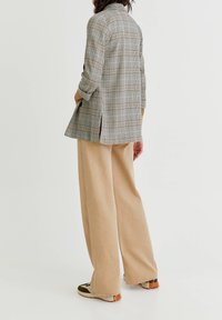 Marynarka w kratę o luźnym kroju, w jasnoszarym i beżowym kolorze, z bocznymi rozcięciami, w zestawie z beżowymi spodniami typu wide-leg i wielokolorowymi trampkami.