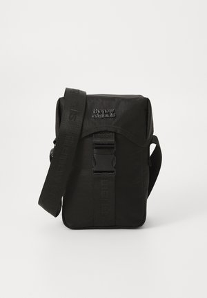 Black nylon messenger bag with a front flap, adjustable strap, and a plastic buckle. Features textured branding on strap and body.