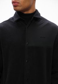 Casaco preto com botões, feito de um material de fleece texturizado, apresentando um painel liso e um pequeno logo "BOSS" no bolso do peito.