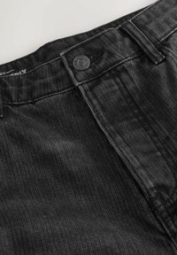 Černé deninové kalhoty s ribbovanou strukturou, vybavené zapínáním na knoflík, poutky na opasek a mírným vyblednutím, které zdůrazňují strukturovaný a ležérní design.