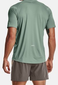 Zielona sportowa koszulka krótki rękaw, gładka tekstura, materiał odprowadzający wilgoć, z prostym wzorem na plecach i małym odblaskowym detalem u dołu.