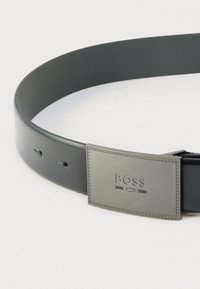Μαύρη δερμάτινη ζώνη με ορθογώνια ασημί μεταλλική αγκράφα με ανάγλυφο το λογότυπο "BOSS". Διαθέτει πολλαπλές τρύπες για ρύθμιση και λεία επιφάνεια.