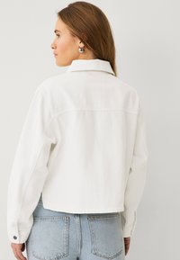 Hvid denimjakke med krave, knapmanchetter og cropped pasform. Stofdet er let tekstureret og komplementerer lyseblå jeans.