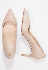 Talons hauts en cuir beige avec un bout pointu, texture lisse et design découpé. Dotés d'un talon fin et d'un subtil accent doré.