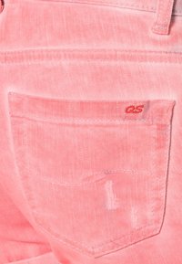 Rosa denimjeans som visar en bakficka med subtil blekning, sydda detaljer och en liten röd logotyp på fickan.