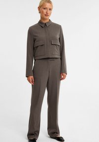 Brun skræddersyet jakkesæt med en cropped jakke, der har to forlommer, og lige bukser. Glat tekstureret stof, minimalistisk design.