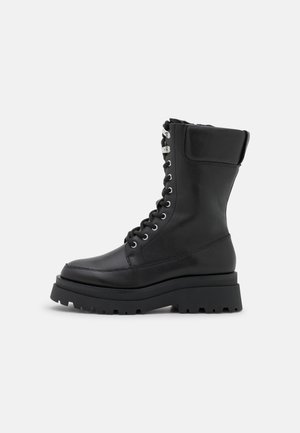 Bota de combate negra de cuero con cordones, suela gruesa y acanalada, y cuello acolchado, mostrada de perfil sobre fondo blanco.