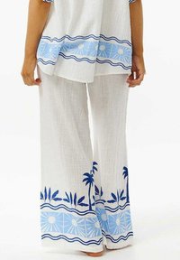Witte, gestructureerde stoffen outfit met een losse top met blauwe details en bijpassende wijde broek met een palmblad- en zonnenpatroon.