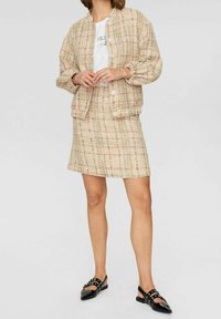 Veste en tweed à manches bouffantes avec boutons, associée à une jupe assortie. Beige doux avec un motif à carreaux multicolores. Chaussures plates noires présentées.