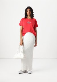 Red cotton T-shirt with graphic design, white textured maxi skirt, white handbag, and white platform sneakers.