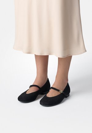 Schwarze Wildleder-Ballerinas verfügen über eine runde Zehenpartie und einen einzelnen Riemen über dem Spann mit einem goldenen Akzent. Die Sohle ist flach für zusätzlichen Komfort.
