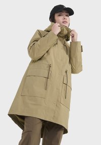 Manteau khaki imperméable avec col haut, capuche à cordon de serrage et grandes poches avant. Comprend une fermeture à pression et un design long et fluide.