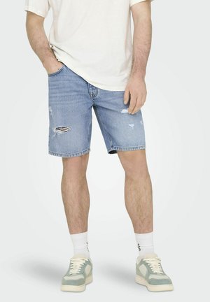 Hellblaue Jeansshorts mit fransigen Kanten und verwaschenen Details, kombiniert mit einem weißen T-Shirt und Sneakers mit grünen Akzenten.