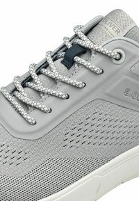 Grauer Sportschuh mit atmungsaktivem Mesh-Obermaterial, Gummisohle, strukturierten Akzenten und gemusterten Schnürsenkeln. Markenlogo auf der Zunge sichtbar.