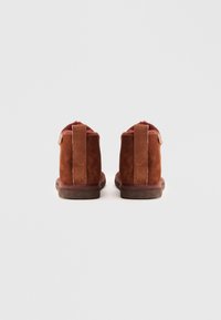 Bottines en cuir suedé marron avec un intérieur douillet, dotées d'une languette lisse et d'une semelle en caoutchouc robuste. Le design à l'arrière comprend des détails de couture.