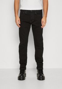 Jeans negros de corte ajustado, con un diseño clásico de cinco bolsillos, piernas rectas y costuras en contraste, combinados con botas negras.