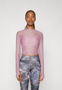 Hellblaues langärmeliges Oberteil mit figurbetontem Schnitt und transparenter Einsätze, kombiniert mit hochtaillierten Leggings mit einem mehrfarbigen abstrakten Muster.