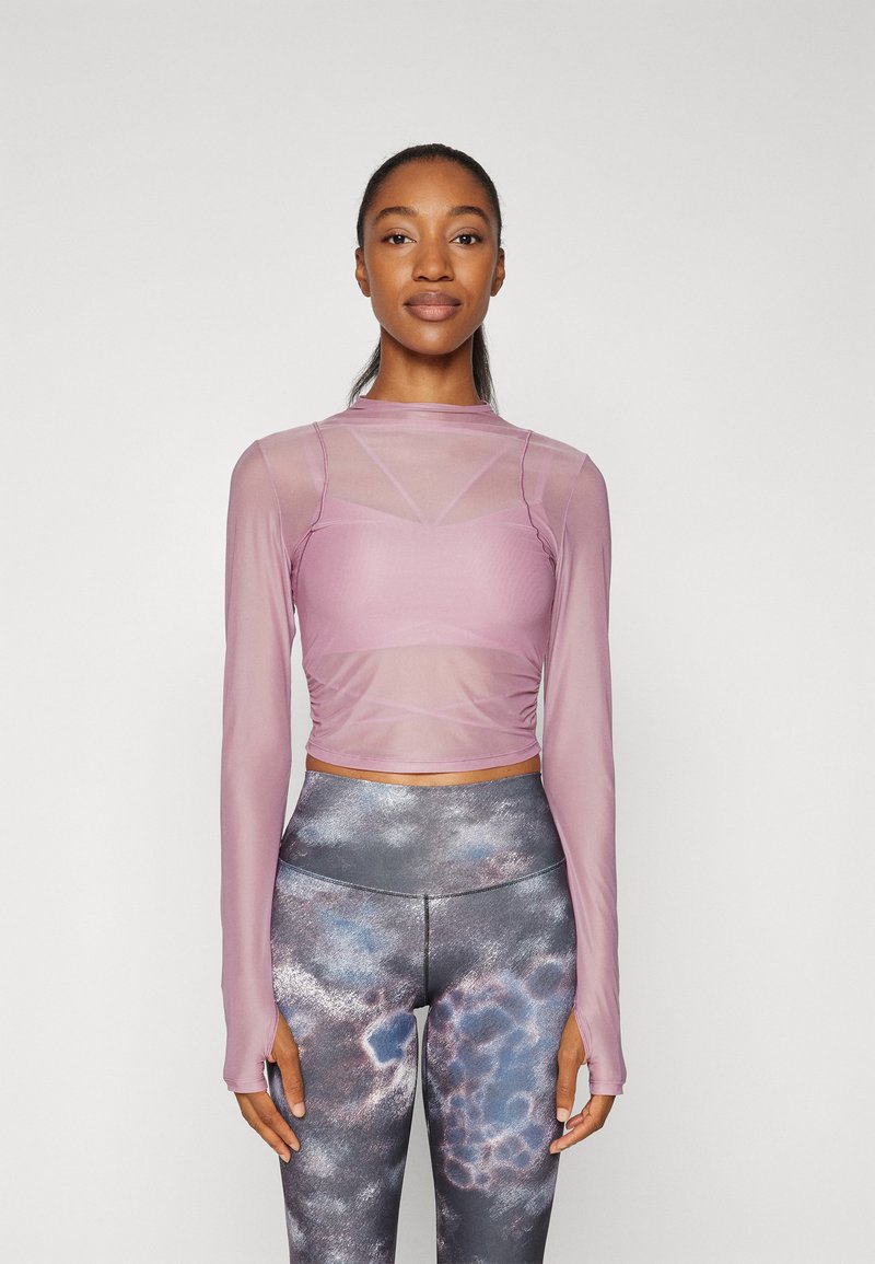 Hellblaues langärmeliges Oberteil mit figurbetontem Schnitt und transparenter Einsätze, kombiniert mit hochtaillierten Leggings mit einem mehrfarbigen abstrakten Muster.