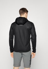 Giacca nera con cappuccio, realizzata in un tessuto liscio, con un logo sulla schiena e pantaloni corti grigi a contrasto. Tasche laterali con zip.