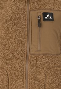 Braune Fleecejacke mit einem vertikalen Reißverschluss, einer mit Reißverschluss versehenen Brusttasche mit schwarzen Zippern und einem Whistler-Logo-Patch.