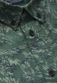 Zelená košile na knoflíky s texturovanou tkaninou, zdobená botanickým vzorem ve tmavších odstínech, černými knoflíky a standardním límcem.