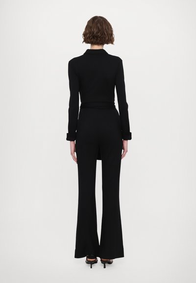 Salopette noire à manches longues, taille cintrée et jambes évasées. Tissu lisse, design minimaliste et détails de col ajusté.
