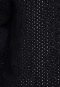 Tissu tricoté noir avec un motif texturé comportant de petits trous espacés régulièrement, offrant un mélange d'épaisseur et de respirabilité.