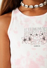Top bianco a coste con accenti rosa tie-dye e una stampa grafica con fiori. Completo con un collier a conchiglia bianco.