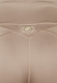 Leggings athletic beige con una texture morbida e liscia. Presentano un logo dorato e cuciture a contrasto lungo l'elastico in vita e le cuciture laterali.
