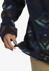Fleece-Pullover in Dunkelblau mit geometrischen Mustern in Grün und Braun. Verfügt über einen Zugbandsaum und einen lockeren Schnitt mit langen Ärmeln.