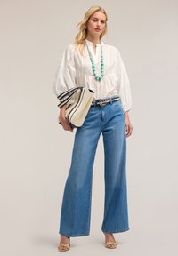 Bluză albă, texturată, cu un croi lejer și pliseuri, combinată cu blugi largi, cu talie înaltă, de culoare albastră. Accesorii cu un colier din mărgele albastre și o poșetă.