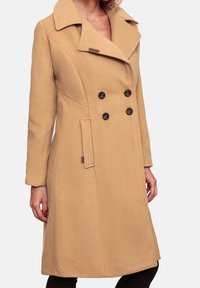 Beige dubbelzijdige jas van zachte stof, met een brede kraag, zwarte knopen en zijzakken. Tailored fit met naden details.
