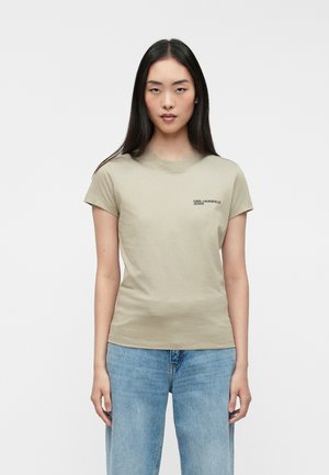 T-shirt en coton vert olive à manches courtes et col rond. Présente un petit logo noir sur la poitrine. Associé à un jean en denim bleu clair.