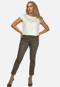 Biała bluzka krótki rękaw z okrągłym dekoltem i subtelnym detalem w postaci zakładki, w połączeniu z dopasowanymi oliwkowymi spodniami i czarnymi szpilkami.