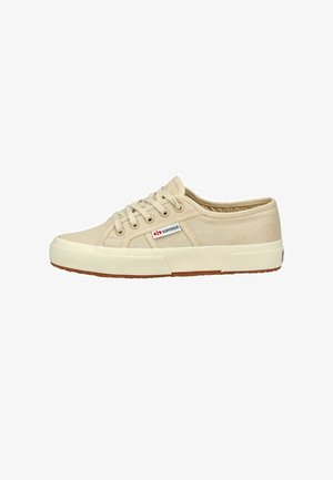 Beige canvas sneakers with round toe, lace-up design, rubber sole, and branded patch on the side. Textured fabric and flat laces.